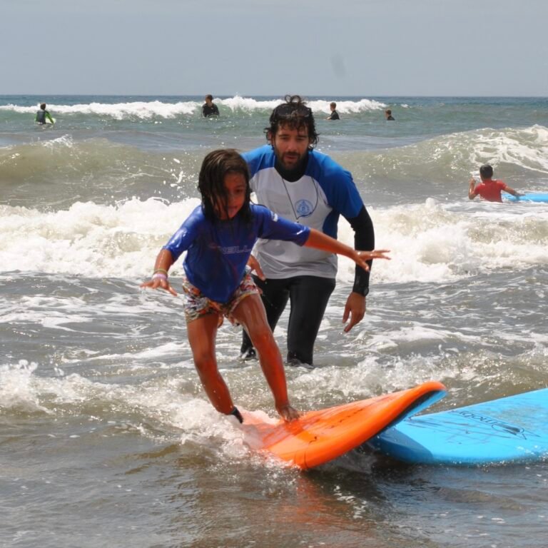 Monitor enseñando surf a una niña en las olas