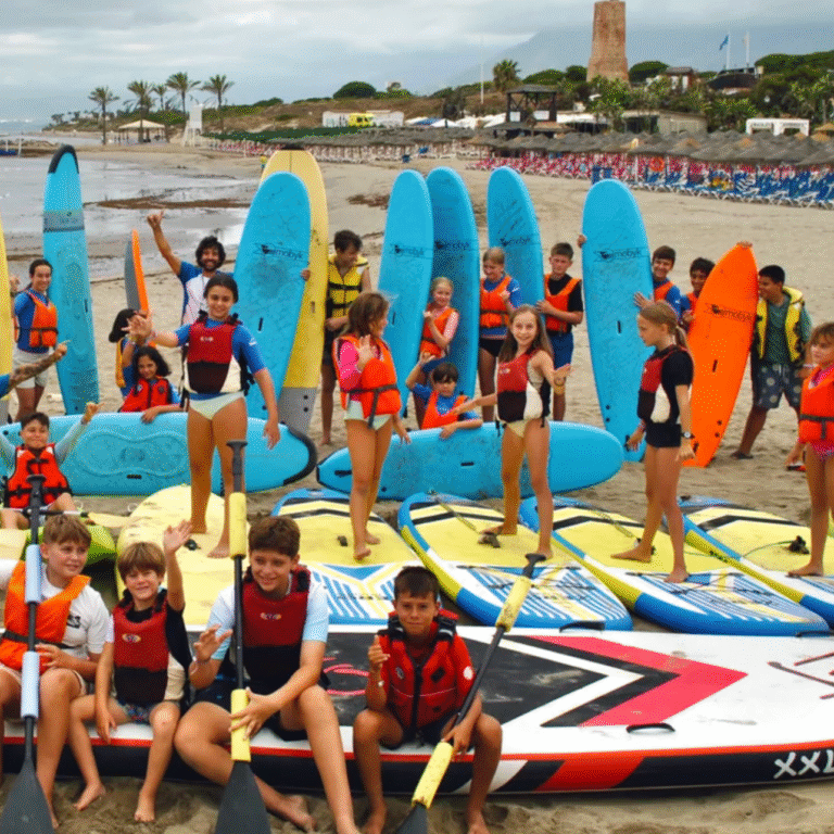 Niños del campamento de verano con tablas de surf y kayaks en la playa de Cabopino