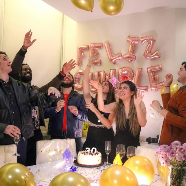 Group of friends celebrating a birthday indoors with balloons and cake.